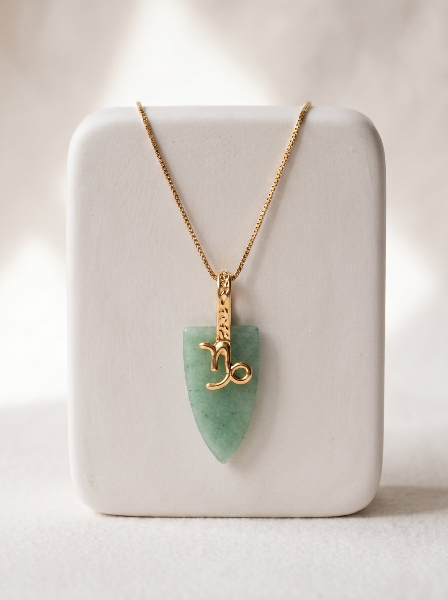 Gold-plated box chain necklace with green agate arrowhead pendant and Capricorn zodiac symbol displayed on a white jewellery stand