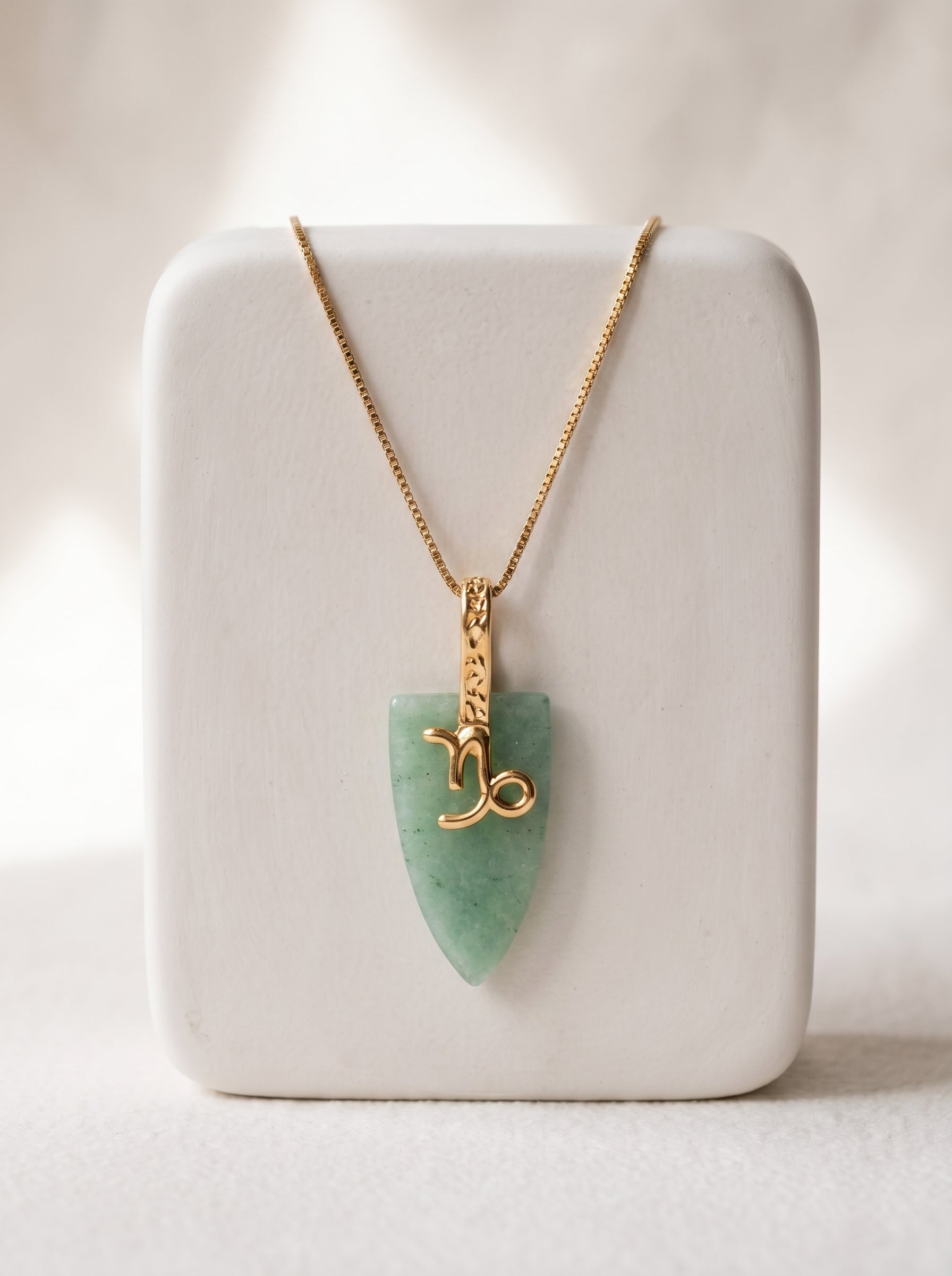 Gold-plated box chain necklace with green agate arrowhead pendant and Capricorn zodiac symbol displayed on a white jewellery stand