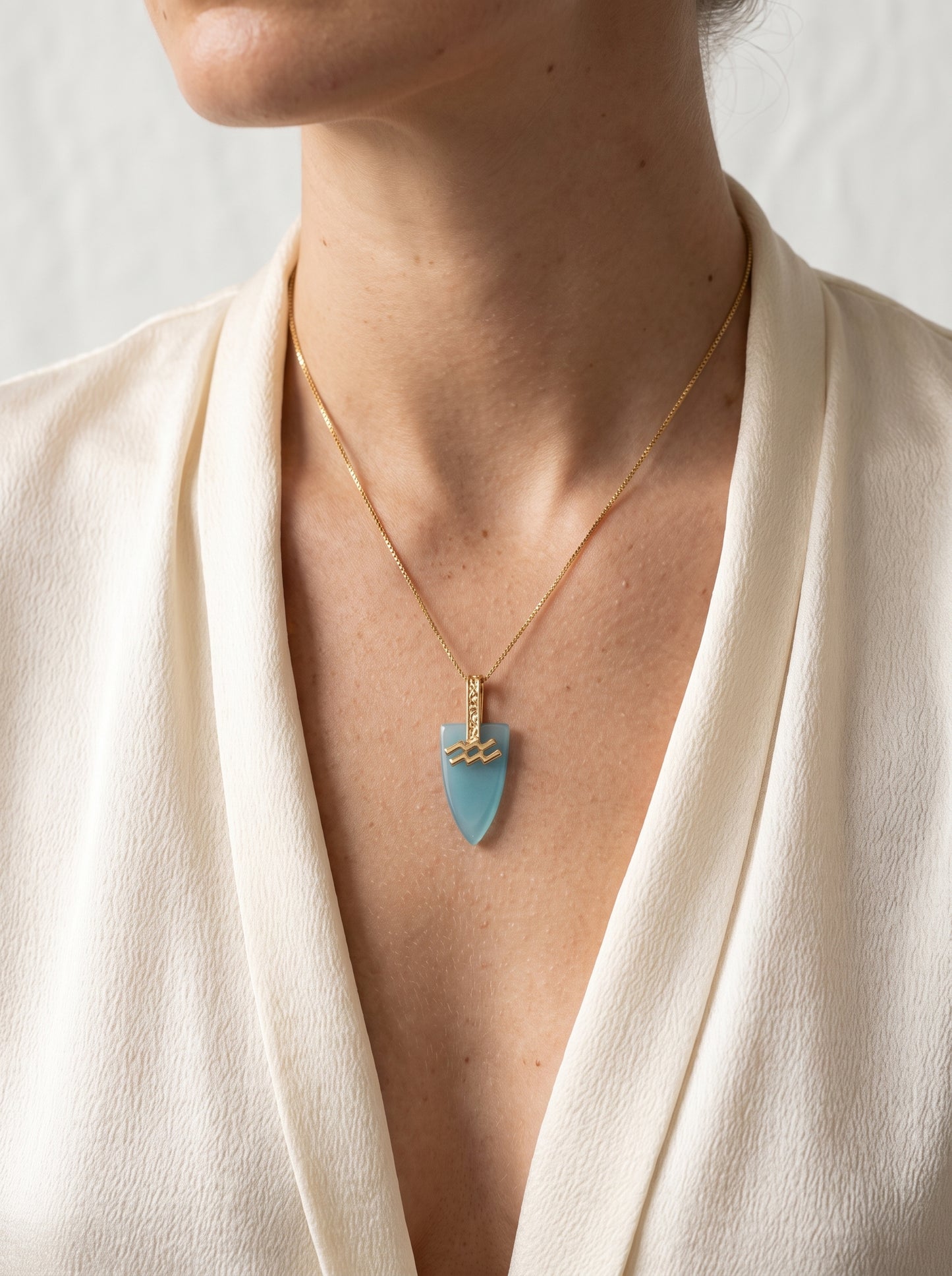 Close-up of gold-plated Aquarius agate arrowhead pendant necklace worn by a woman in a cream wrap top