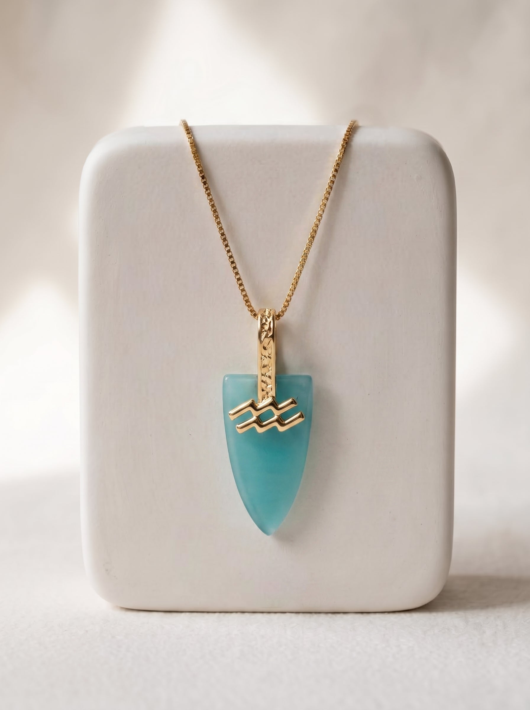 Gold-plated box chain necklace with aqua agate arrowhead pendant and Aquarius zodiac bail displayed on a white jewellery stand