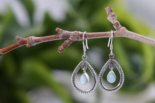 Larimar  gemstone teardrop-shaped earrings with light blue stones on a branch with a natural background