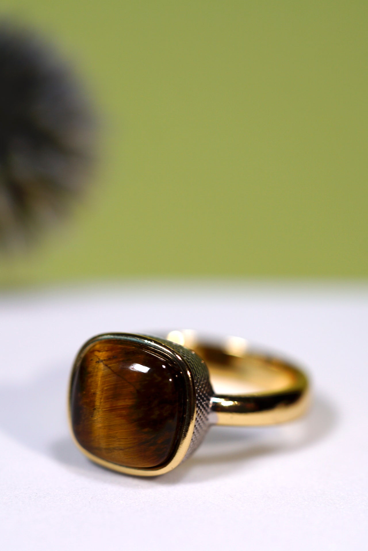 Gold ring  with rhodium plated with a  brown cushion  cut   tigers eye gemstone on a white surface with a green background