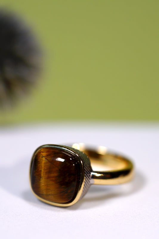 Gold ring  with rhodium plated with a  brown cushion  cut   tigers eye gemstone on a white surface with a green background