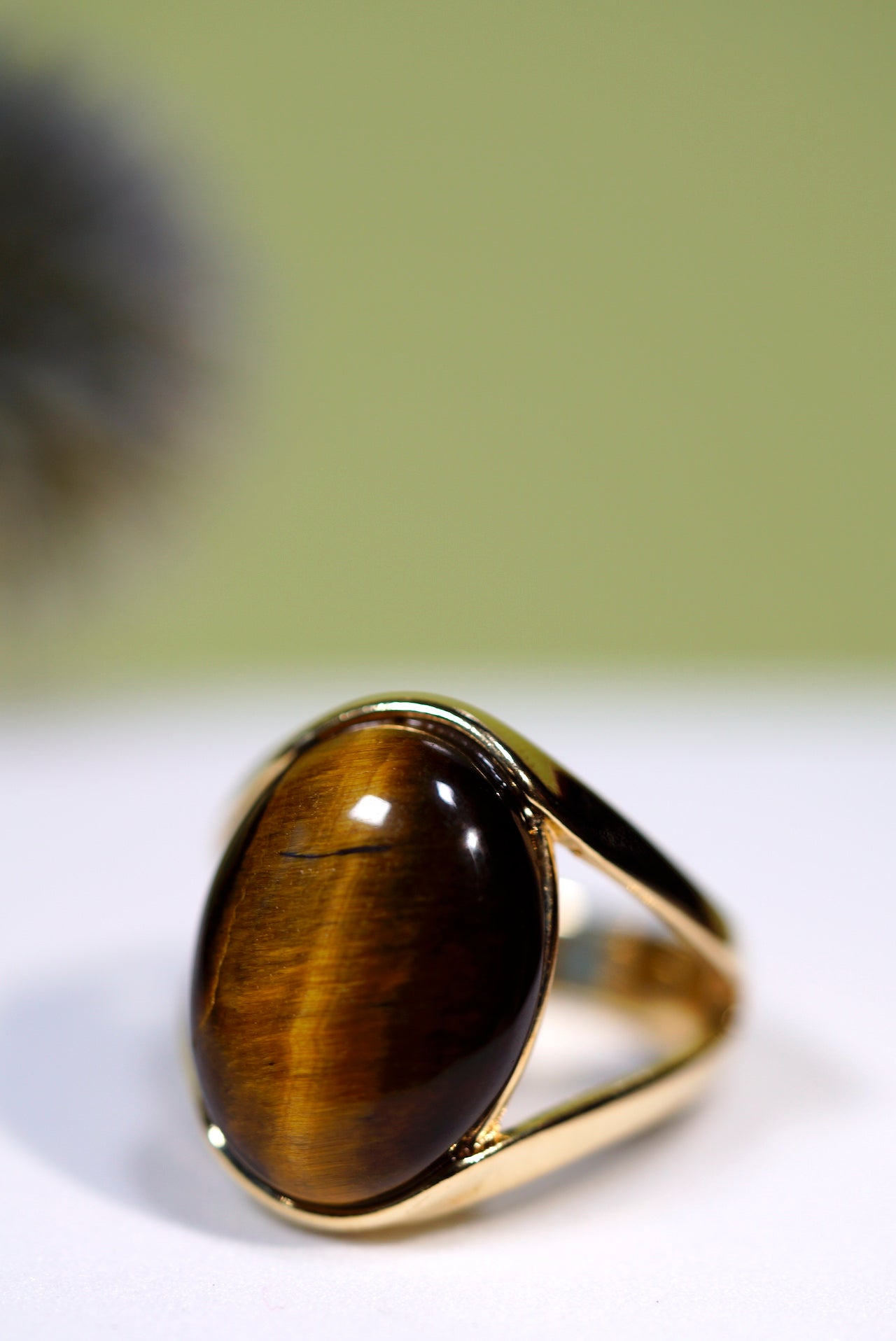 Gold ring with a large oval  brown tigers eye gemstone on a white surface with a blurred green background