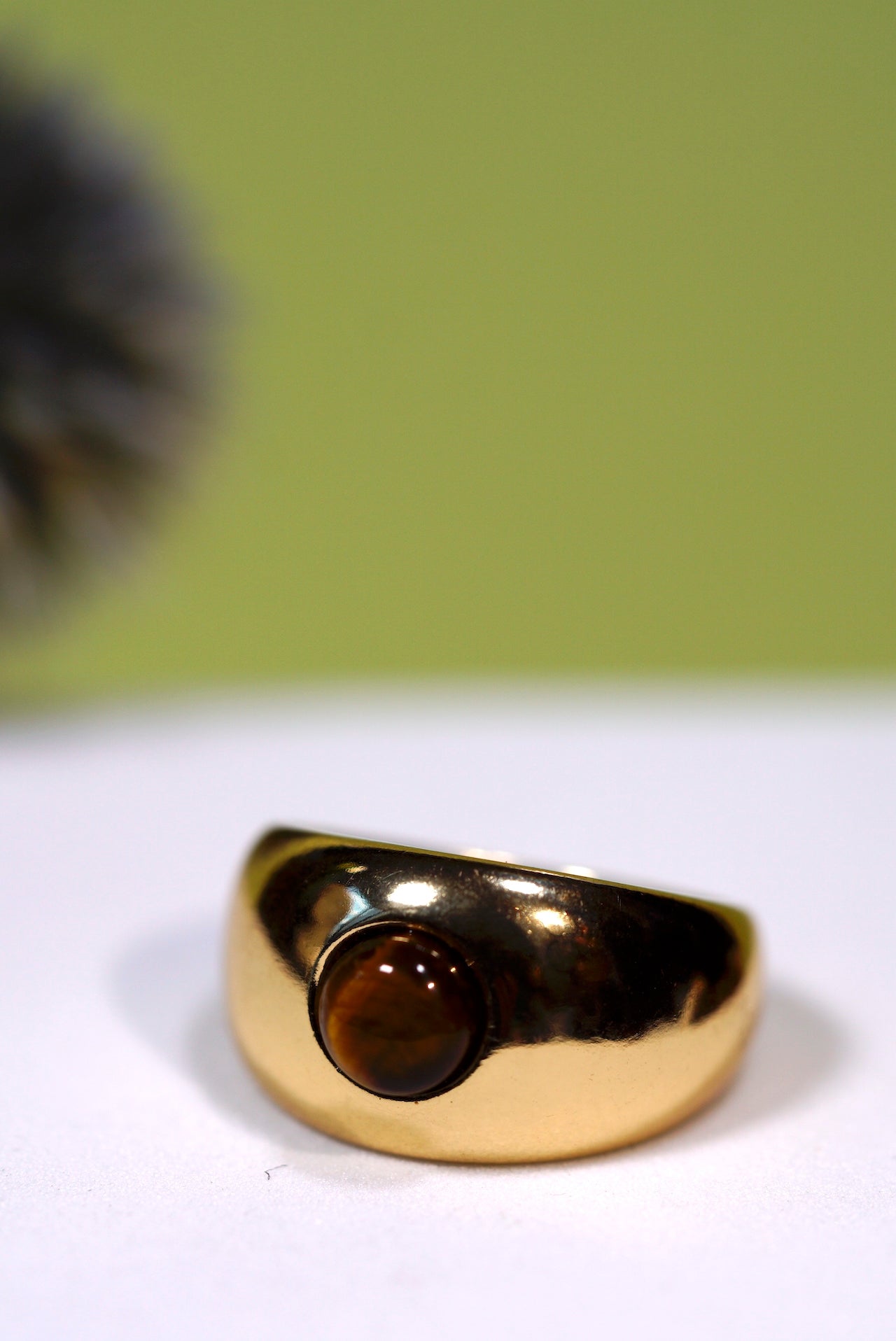 Dome Gold ring with a  small round tigers eye gemstone on a white surface with a green background