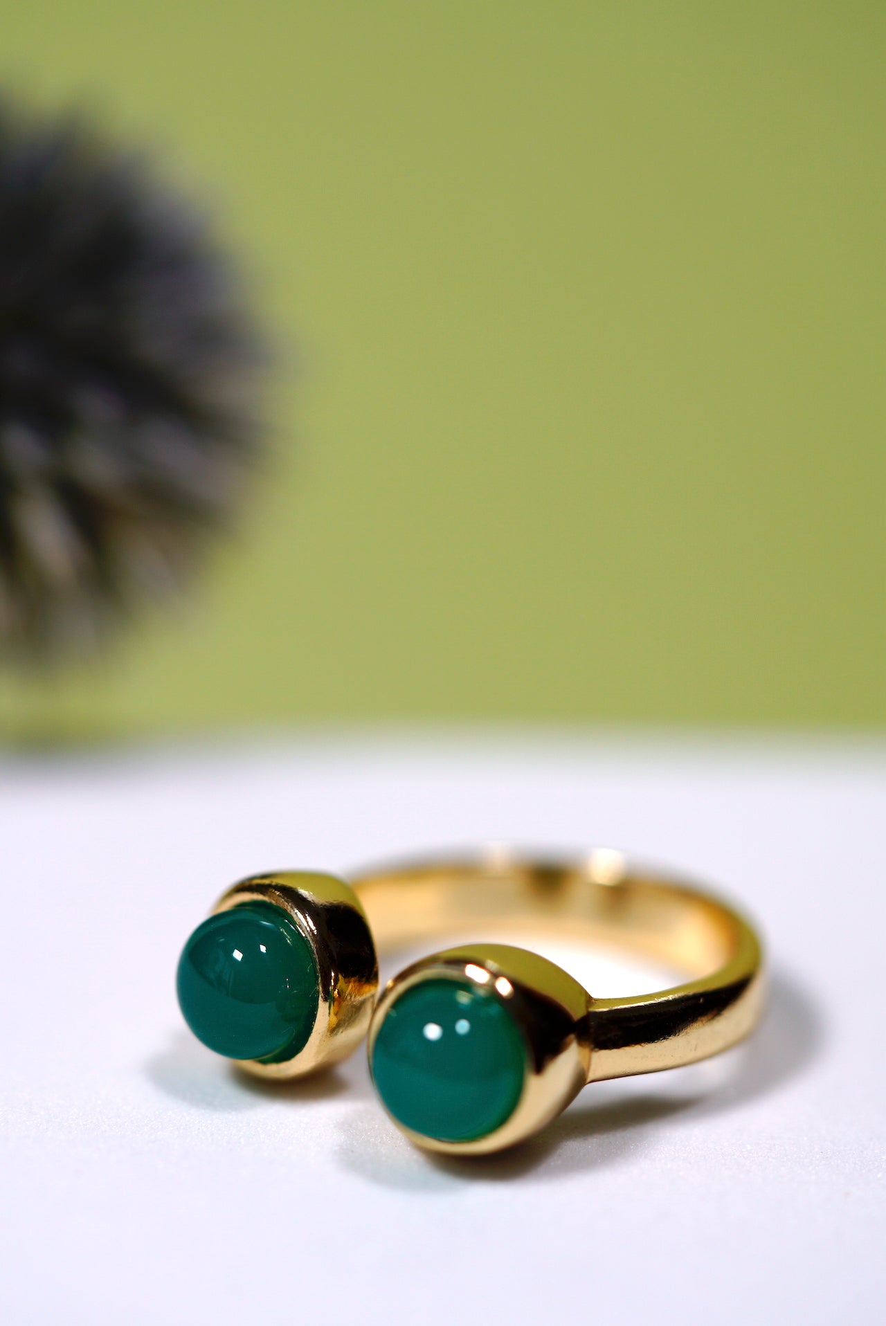 Gold ring with two green agate gemstones on a white surface with a blurred green background