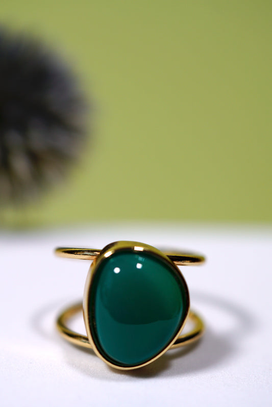 Cuff Gold ring with a green  agate gemstone on a white surface with a blurred background