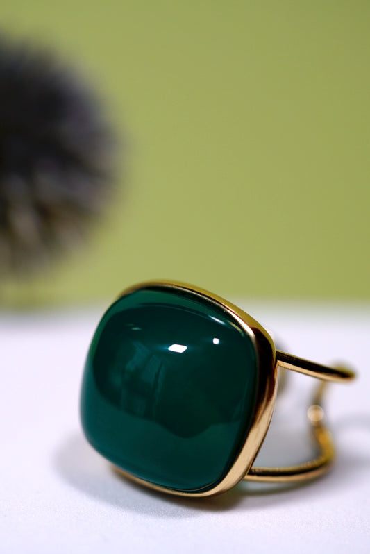 Green  cushion agate ring with gold  cuff band on a white surface with a blurred green background