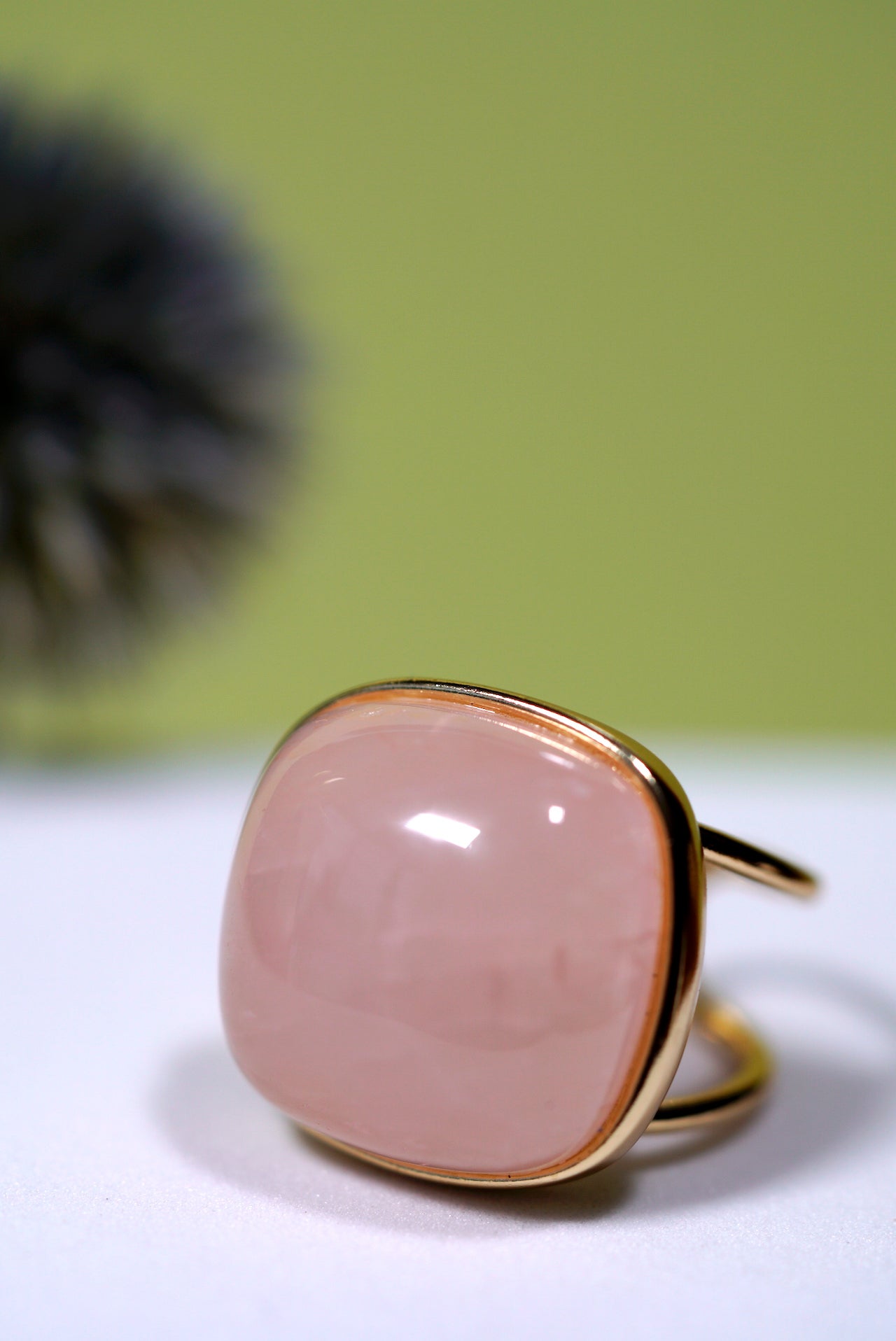 Rose quartz cushion ring with cuff gold band on a white surface with a green background