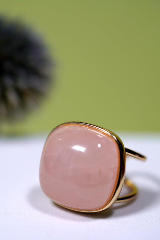 Rose quartz cushion ring with cuff gold band on a white surface with a green background