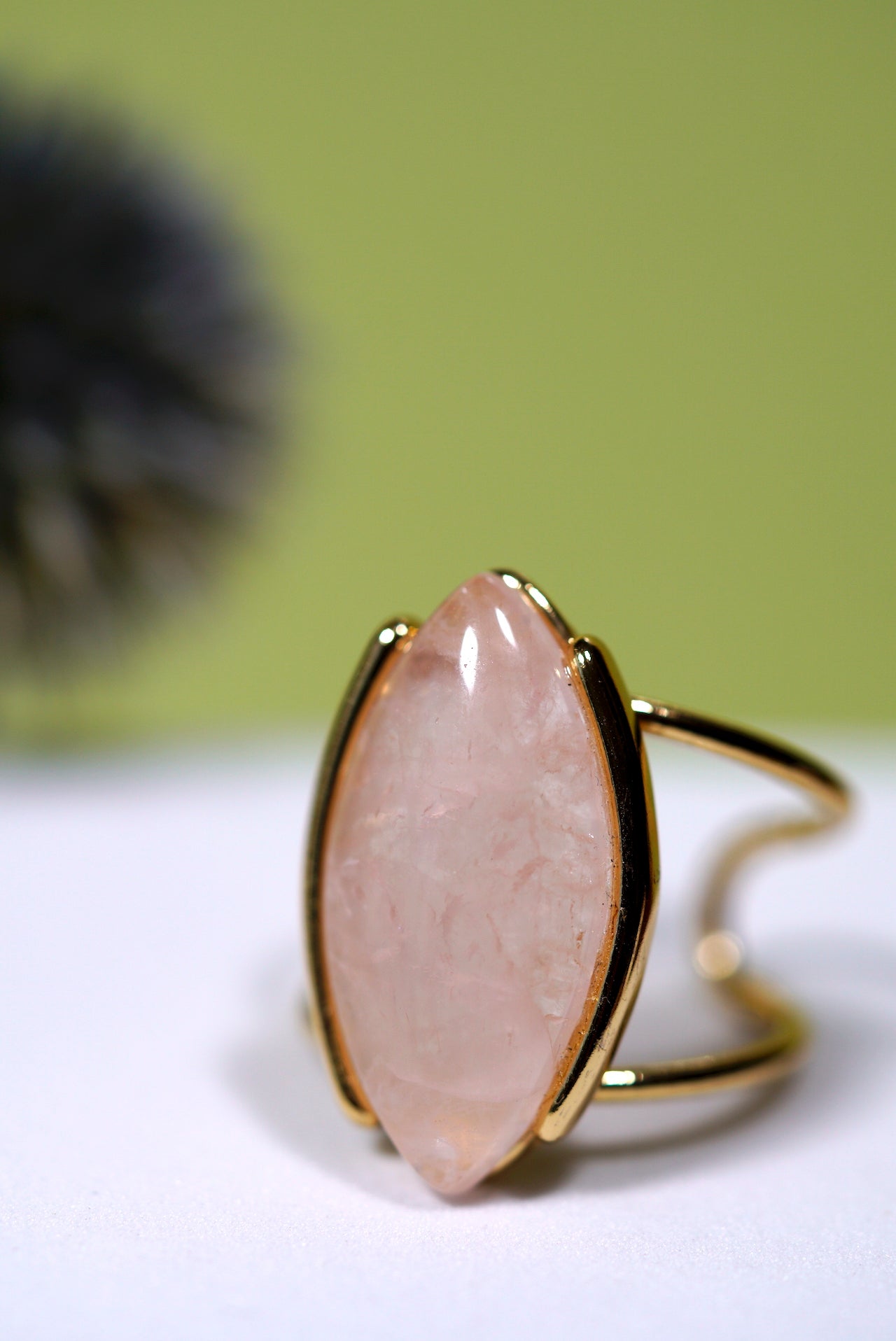 Cuff gold ring with a  rose quartz marquise gemstone on a white surface with a green background