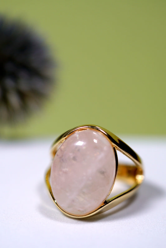 Gold ring with a n oval rose quartz gemstone on a white surface with a green background