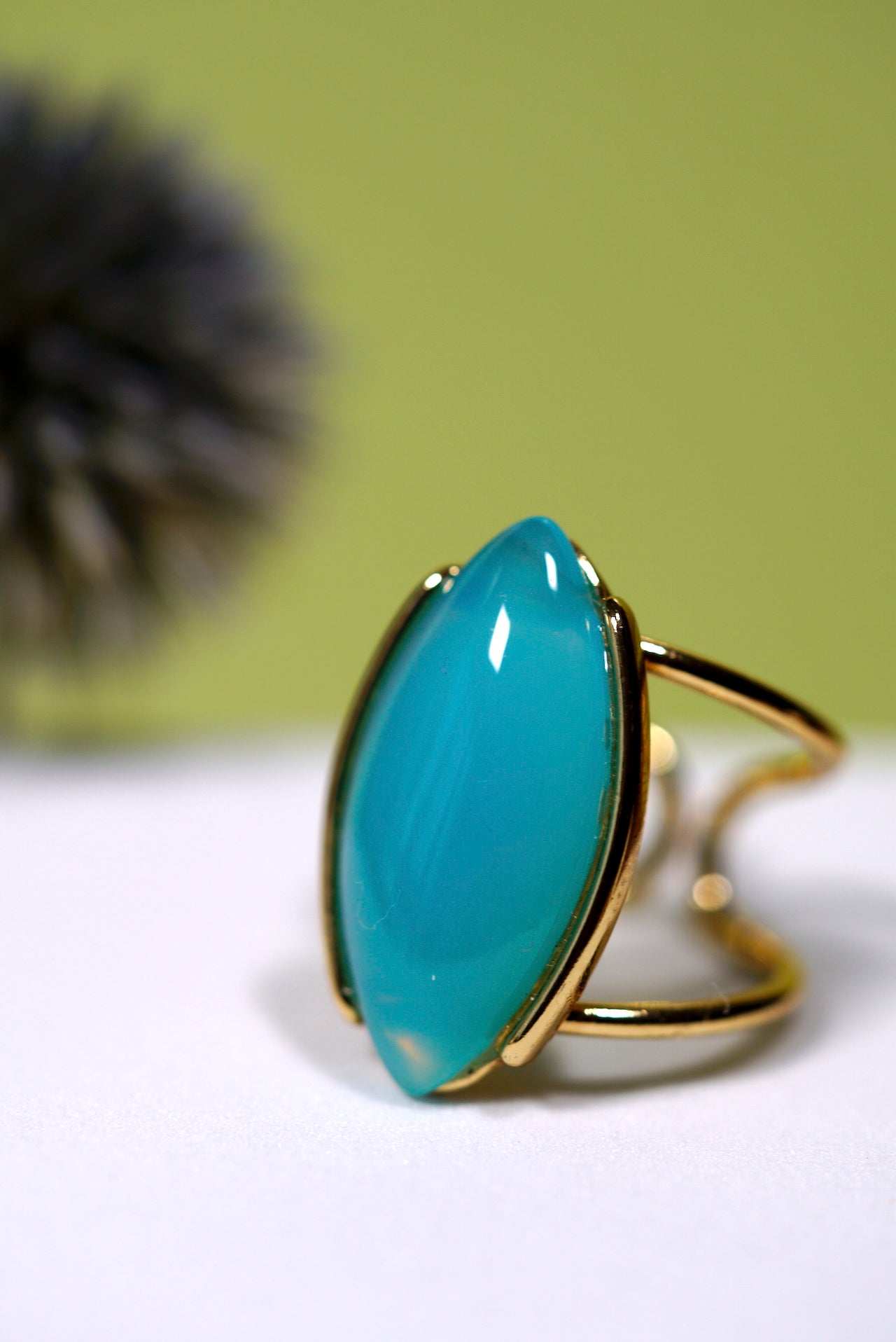 Marquise Teal  aqua agate ring with gold cuff band on a white surface with a green background