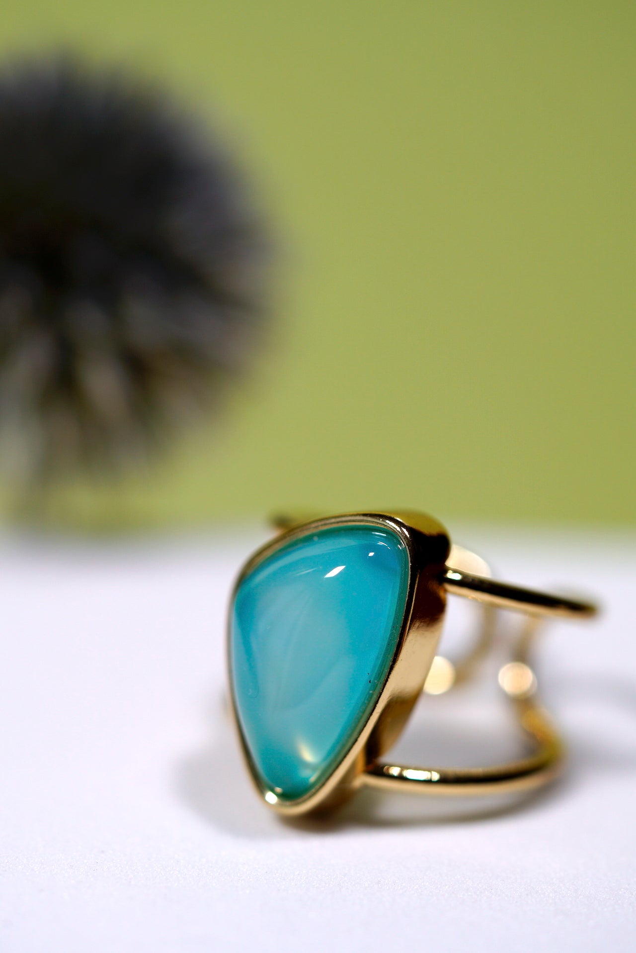 Cuff Gold ring with an aqua agate gemstone on a white surface with a blurred green background
