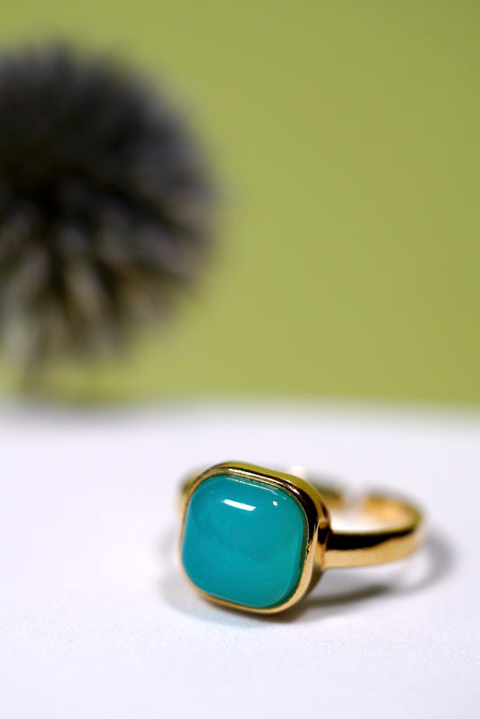 Gold ring with a aqua cushion agate gem stone on a white surface with a blurred green background