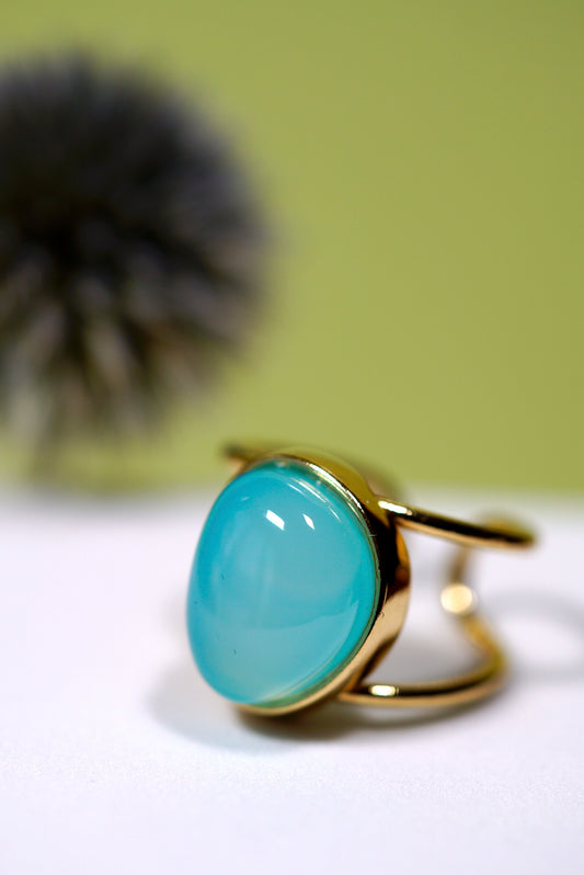 Cuff Gold ring with an aqua agate gemstone on a white surface with a blurred green background