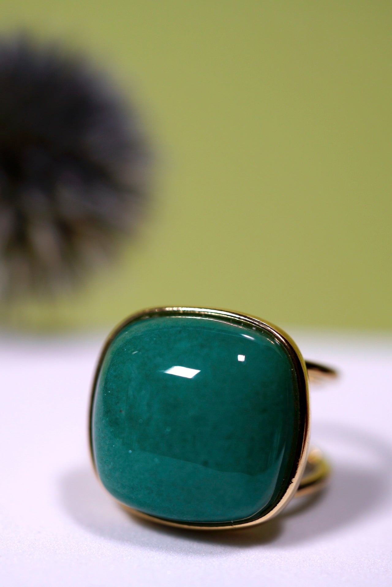 Cuff cushion green agate  cabochon gemstone ring with gold band on a white surface with a blurred green background