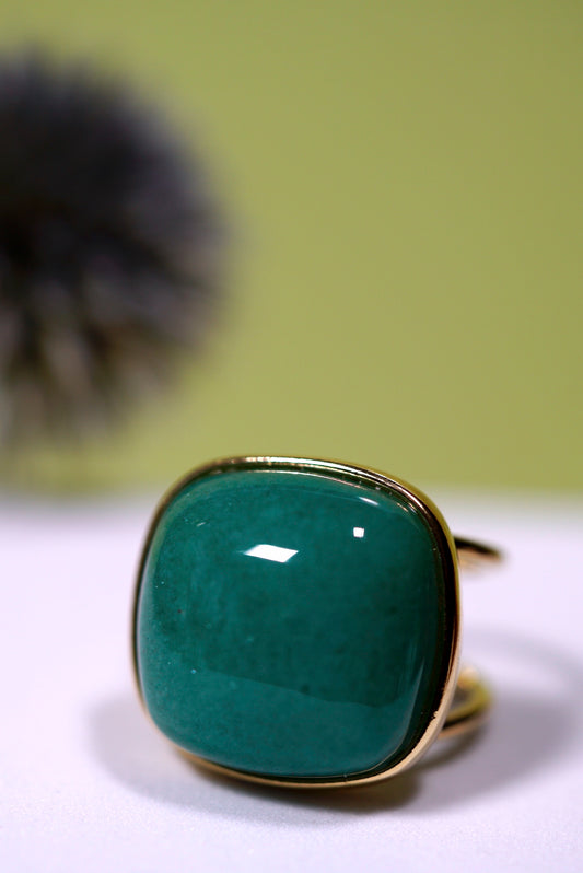 Cuff cushion green agate  cabochon gemstone ring with gold band on a white surface with a blurred green background
