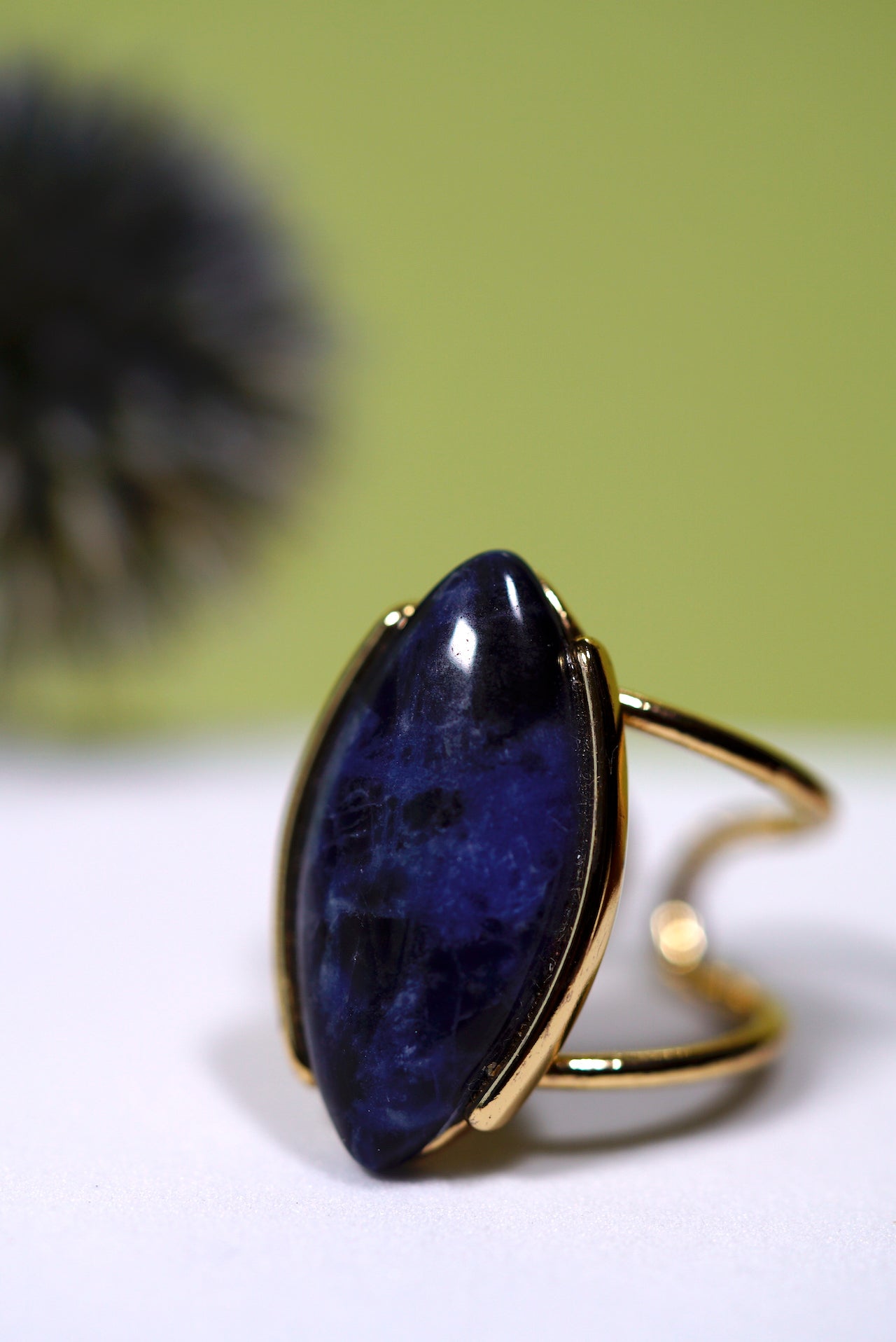 Cuff gold ring with a large blue sodalite gemstone on a white surface with a green background