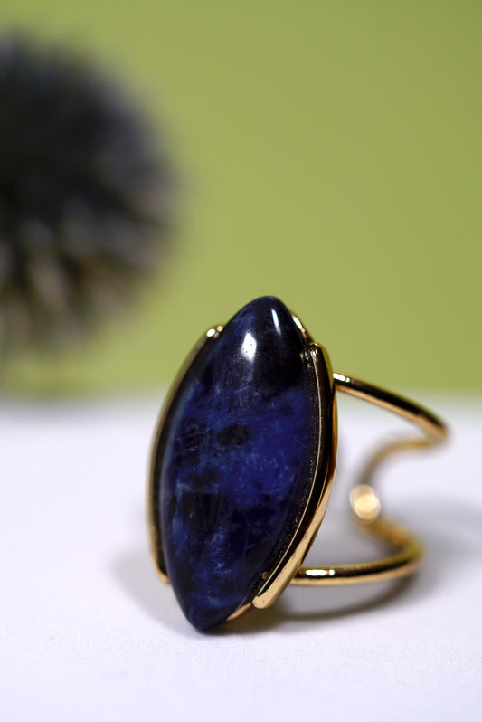 Cuff gold ring with a large blue sodalite gemstone on a white surface with a green background