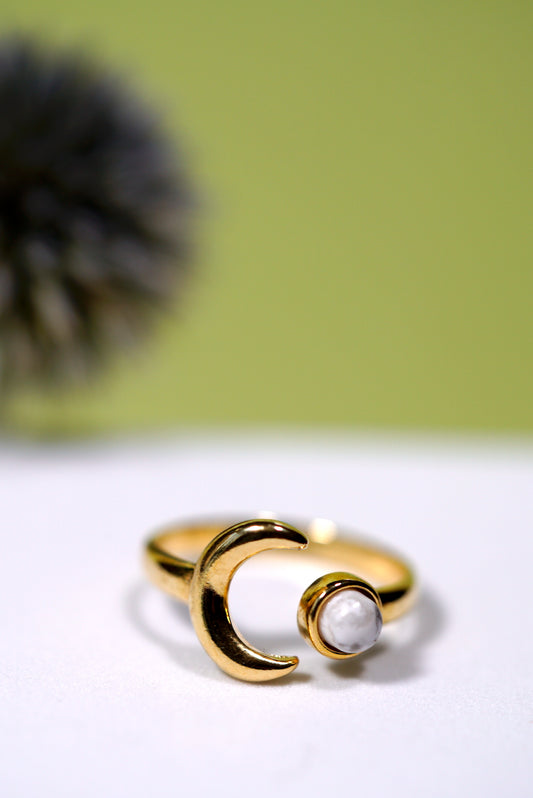 Adjustable Gold ring with a moon design and white howlite gemstone on a white surface with a green background