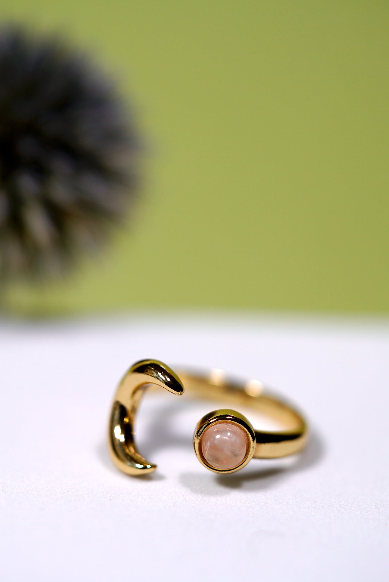 Gold ring with a moon and rose quartz gemstone on a white surface with a green background