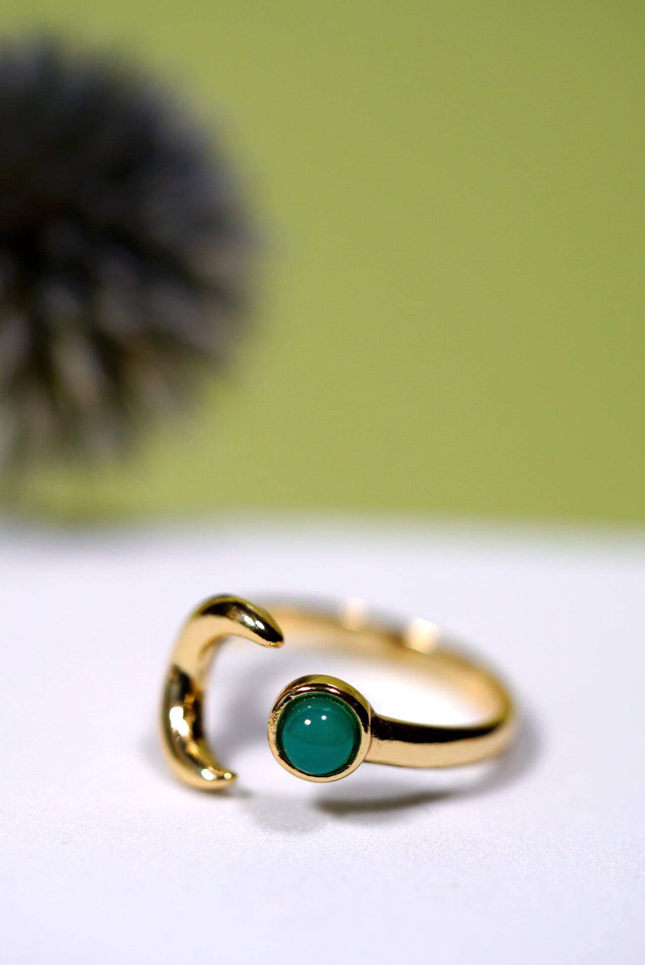 Gold ring with a moon and green agate gemstone on a white surface with a blurred green background