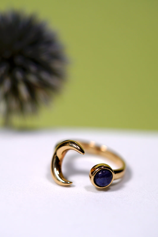 Gold ring with a moon and sodalite blue gemstone on a white surface with a green background