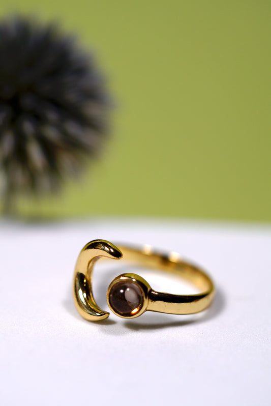 Gold ring with a moon and smoky quartz  gemstone on a white surface with a green background