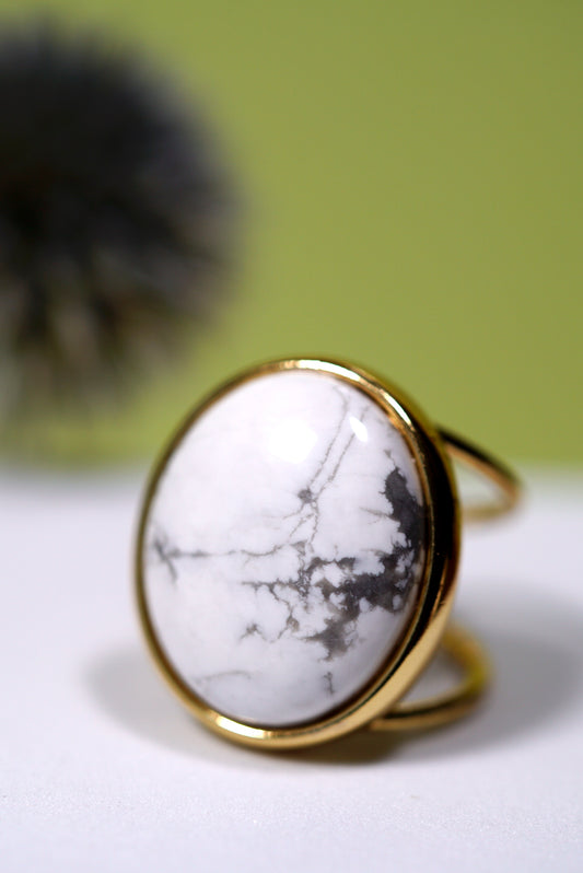 Cuff Ring with an oval white  howlite gemstone and gold band on a light surface with a blurred green background