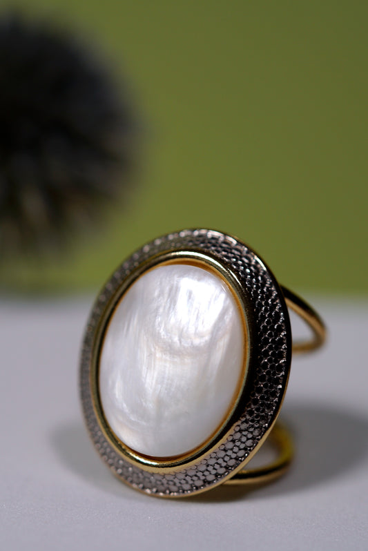 Cuff Gold ring with a large oval  white mother of pearl on a light surface with a blurred green background