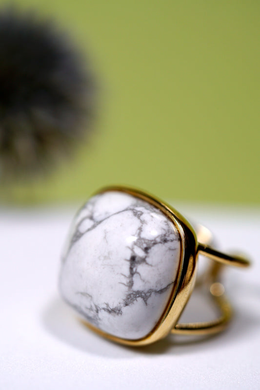 Cuff Gold ring with a square white howlite gem stone on a light surface with a blurred green background