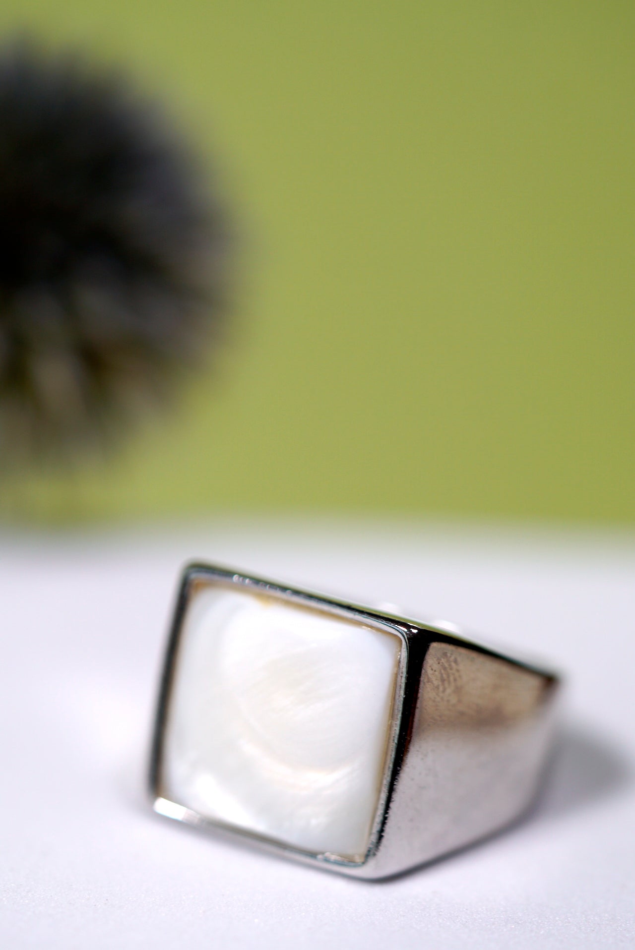 Silver ring with a square mother of pearl in a white surface with a green background