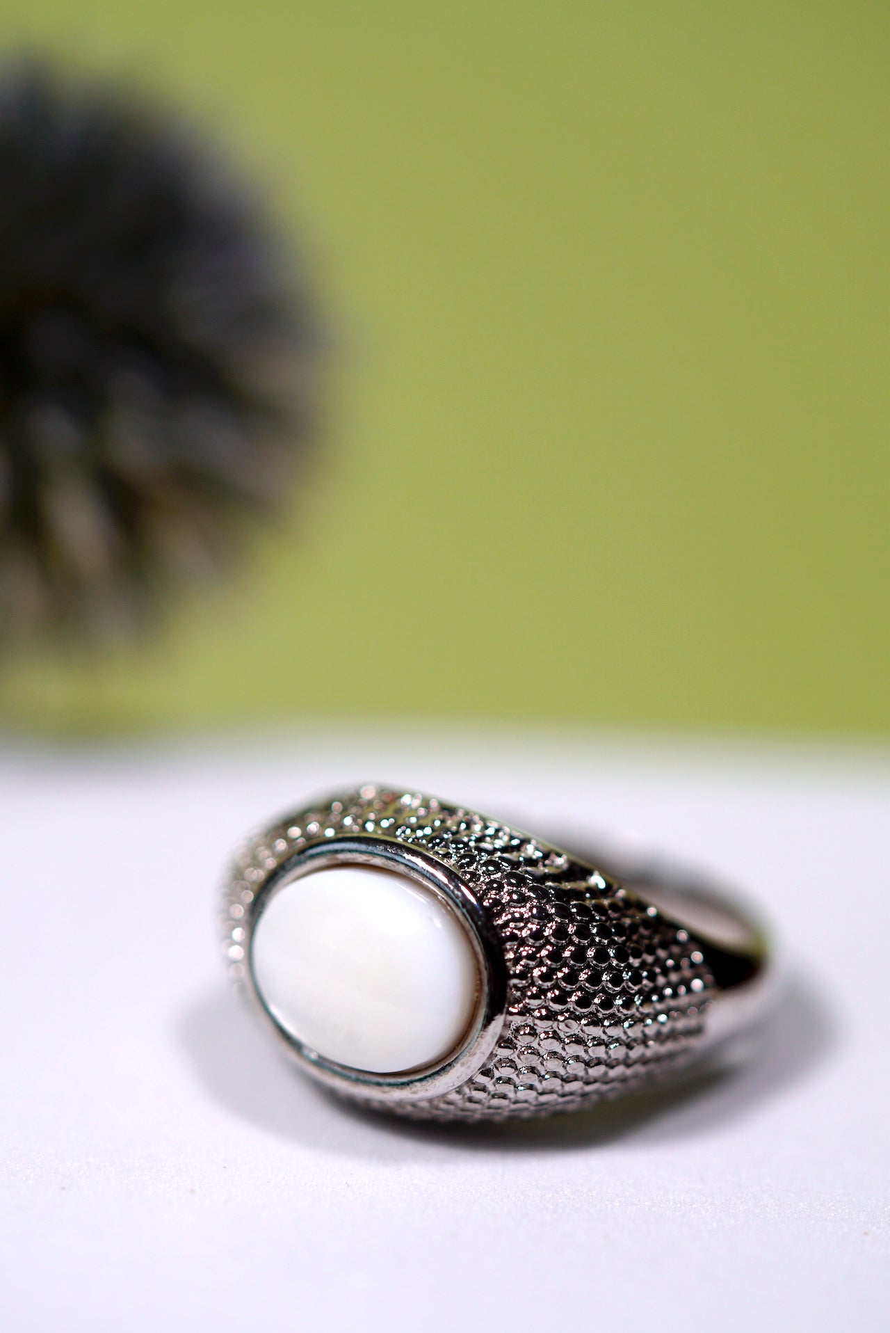 Signet Silver ring with a  mother of pearl white stone on a light surface with a blurred green background