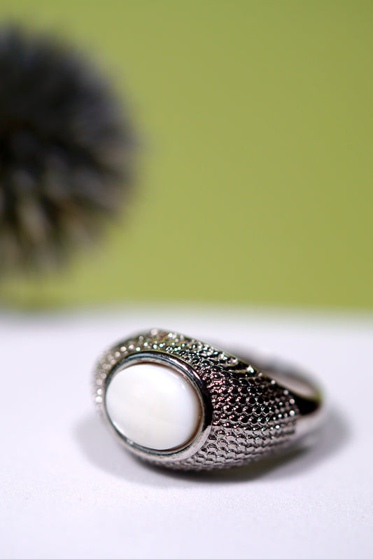 Signet Silver ring with a  mother of pearl white stone on a light surface with a blurred green background