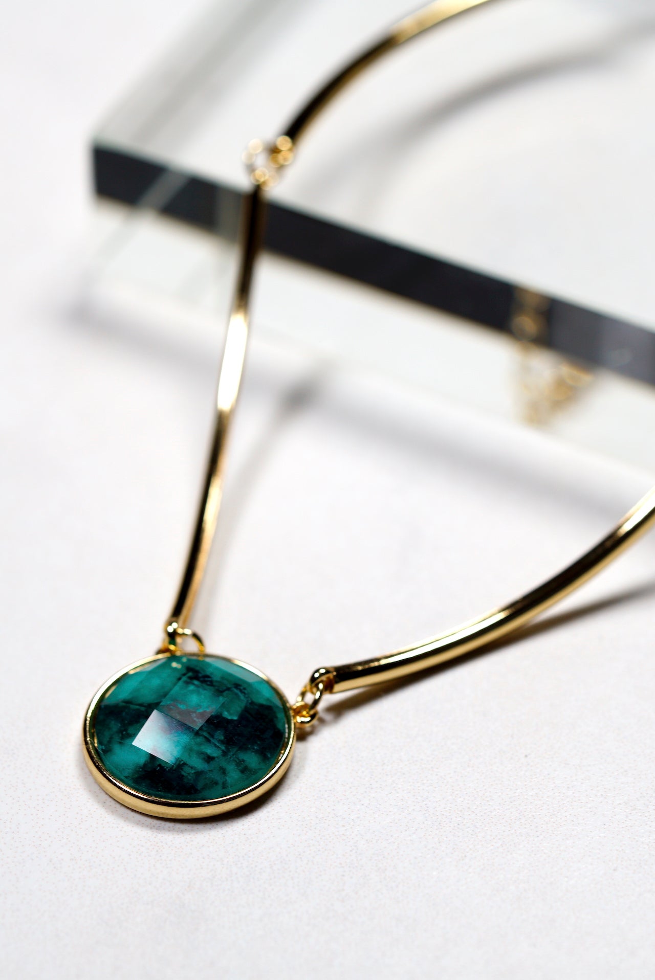 Gold necklace choker  with a green round pendant on a white background