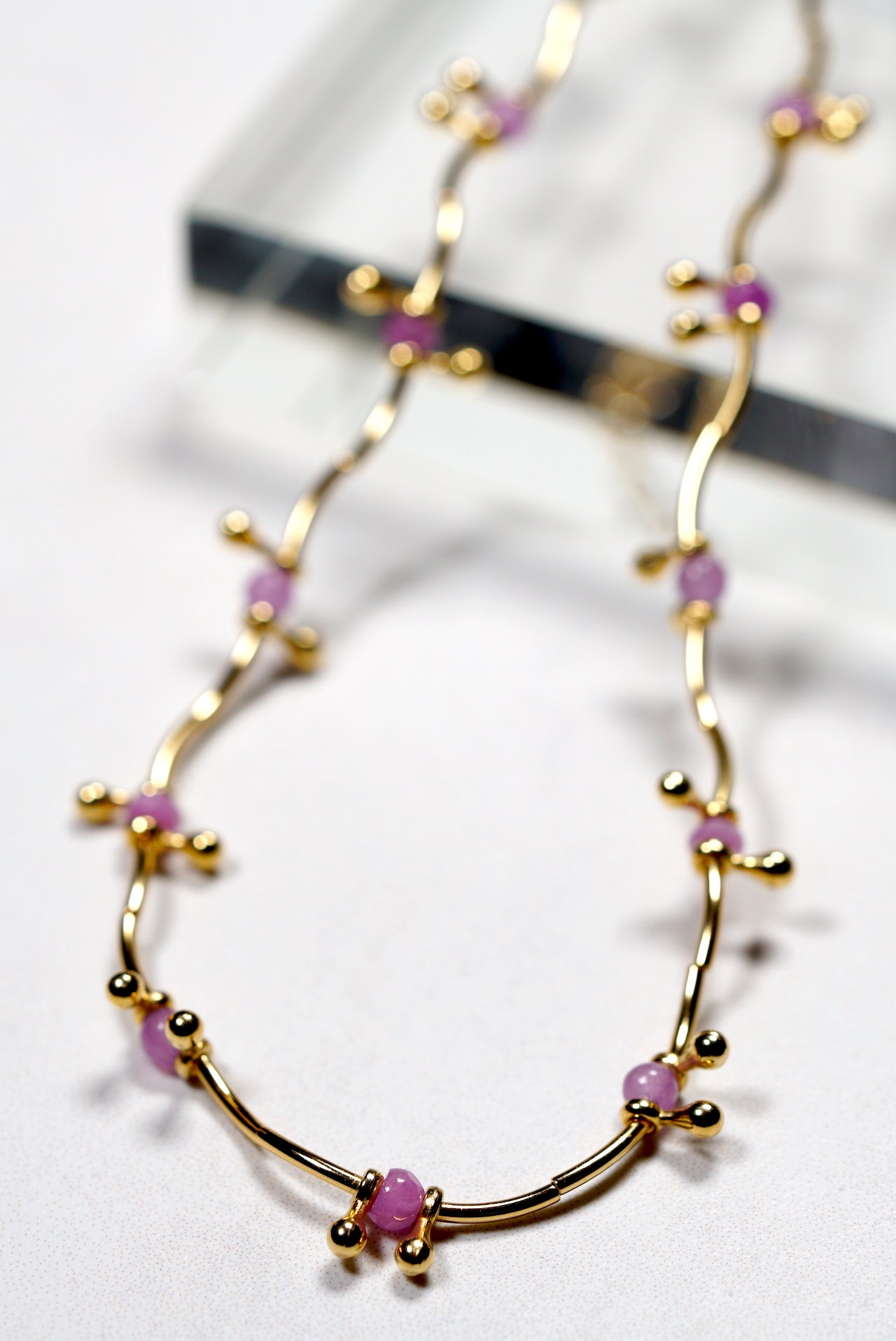 Gold necklace with purple amtethyst beads on a white background