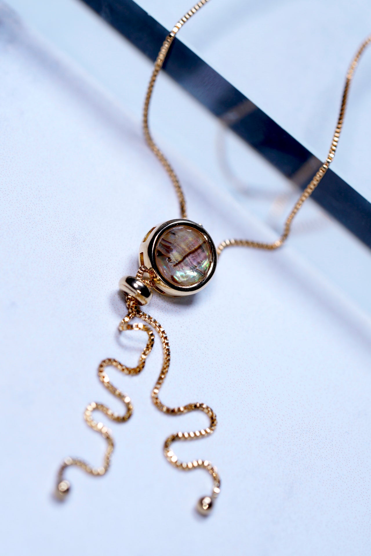 Gold lariat necklace with a abalone pendant on a light blue background