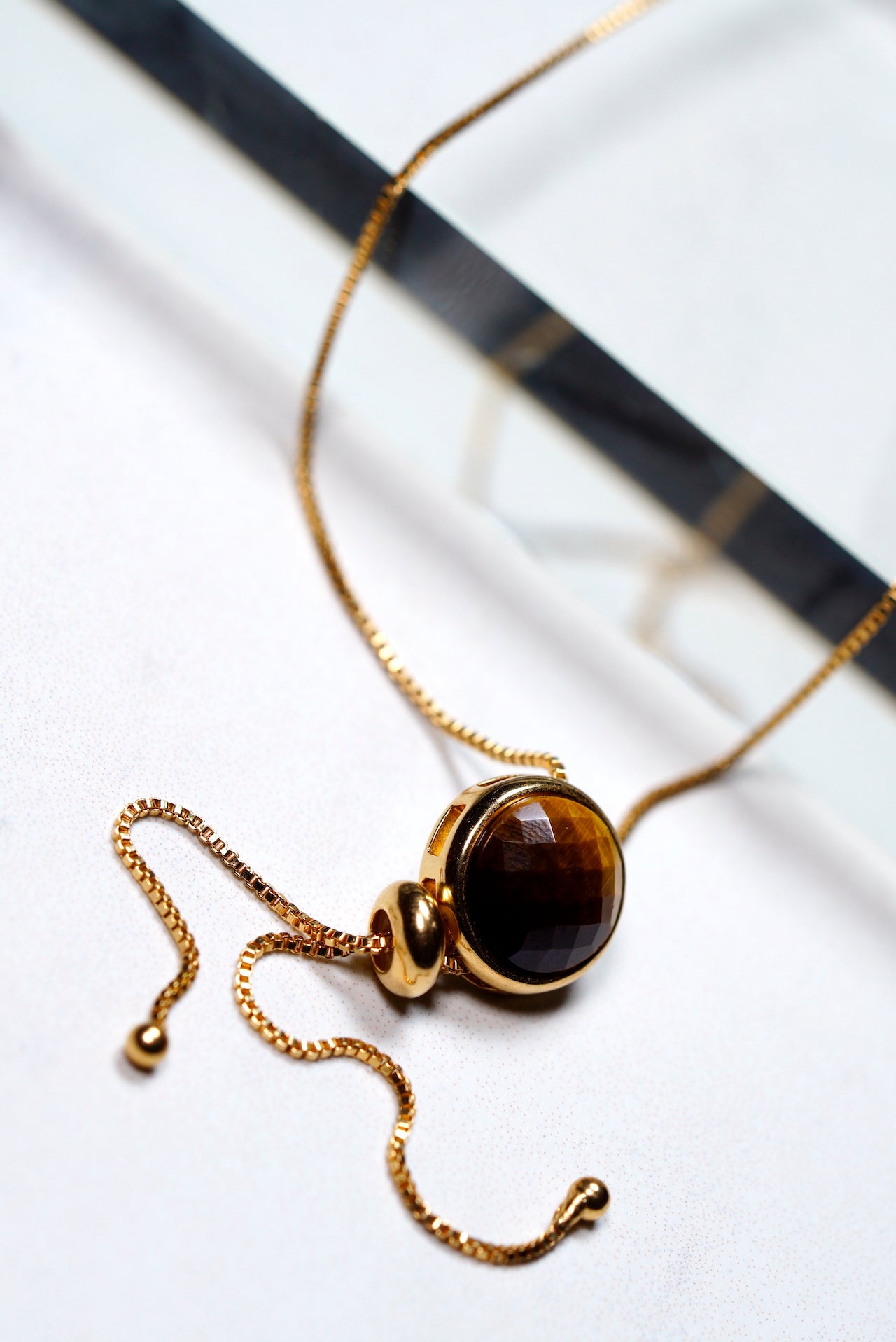 Gold necklace with a brown  tigers eye gemstone pendant on a white background
