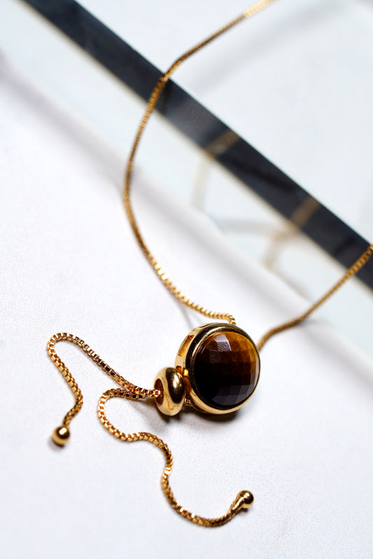 Gold necklace with a brown  tigers eye gemstone pendant on a white background