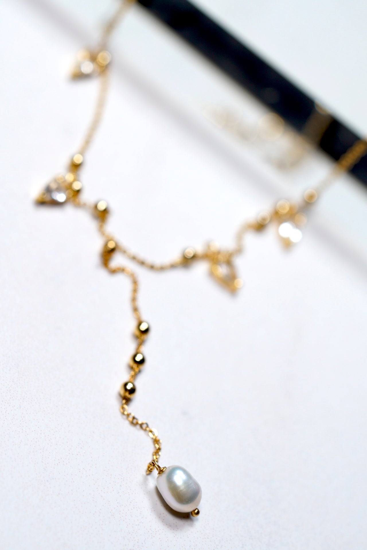 Gold-plated lariat necklace with pearls and gold beads on a white background
