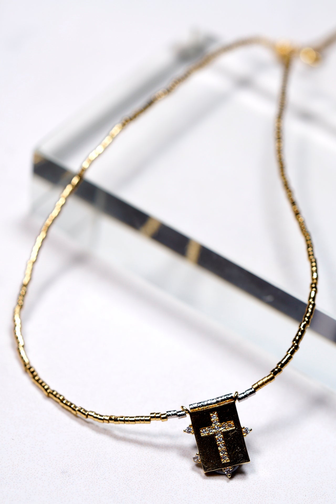 Gold beaded necklace with a cross rectangular pendant on a white background