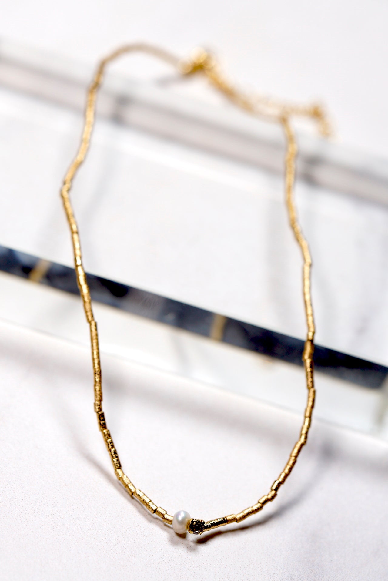 Gold -plated beaded necklace with a small  pearl and crystal pendant on a white background