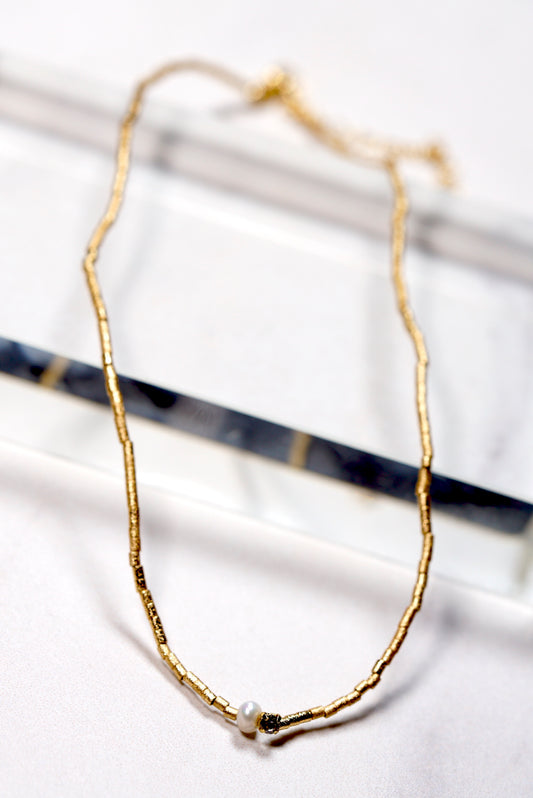 Gold -plated beaded necklace with a small  pearl and crystal pendant on a white background