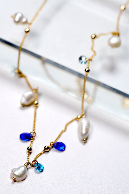 Delicate gold-plated necklace with blue beads and pearls on a white background