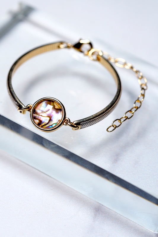 Gold and rodium bracelet with a circular gemstone abalone on a white background