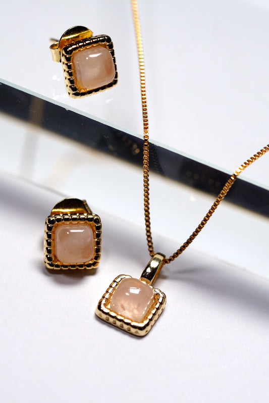 Jewellery set with gold chain, rose quartz  hammered square dainty pendant, and rose quartz  hammered square stud earrings on a reflective white surface.