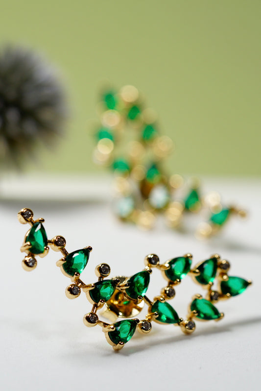 Gold and green stud earrings on a white surface with a blurred background