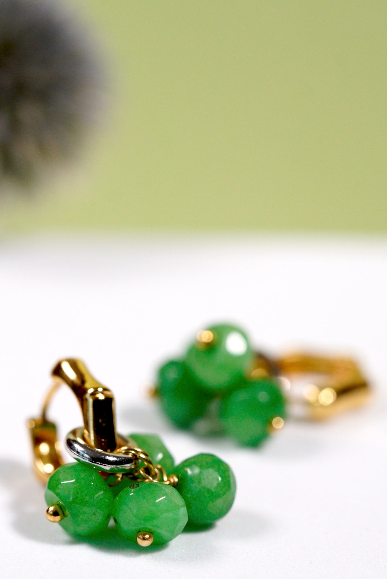 Green beaded earrings with gold accents on a white surface.