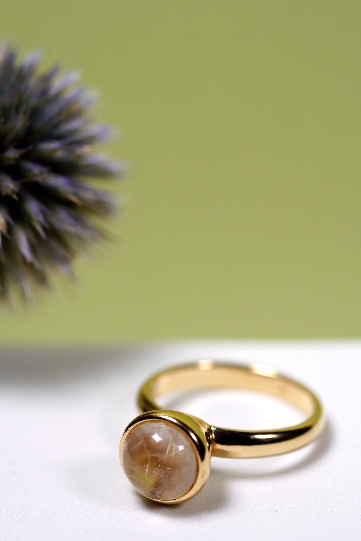 Gold ring with a  quartz round stone on a white surface with a green background